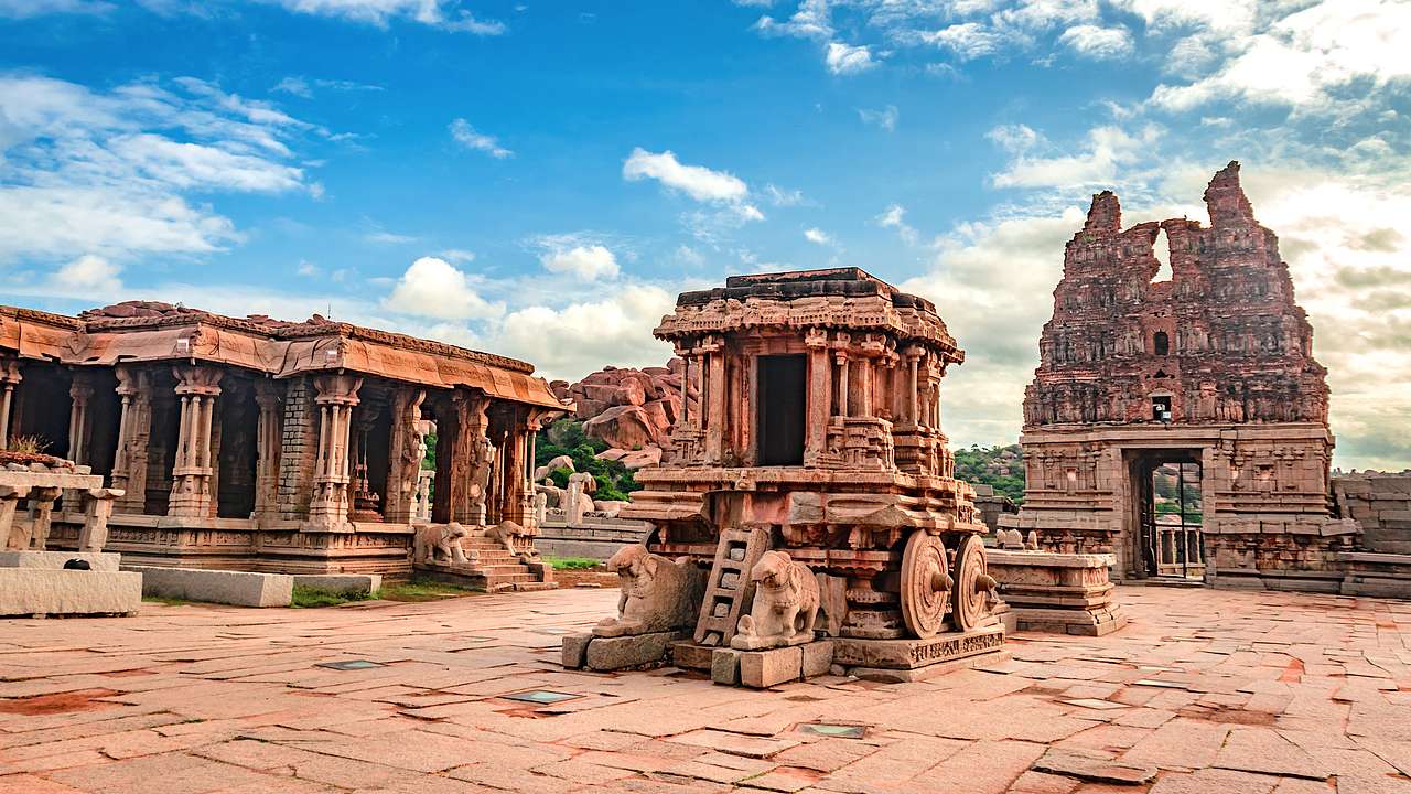 Three ancient, carved, reddish sandstone structures against a partially cloudy sky