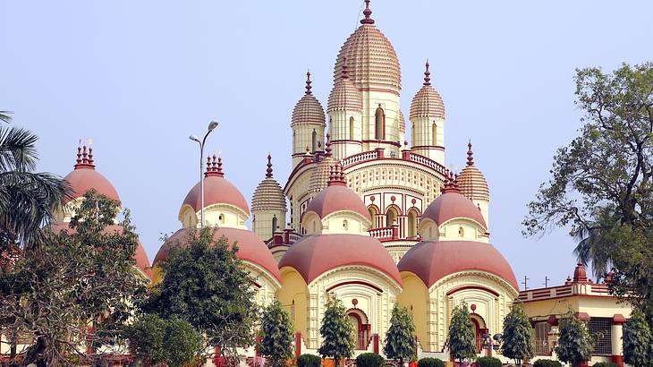 A red and white temple with pointy domes surrounded by lush green trees