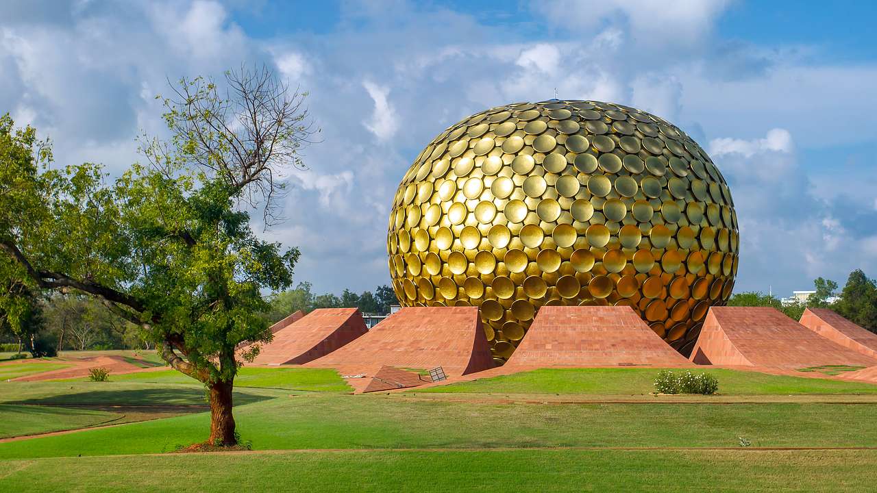 A golden sphere temple building with a lone green tree and green grass in front