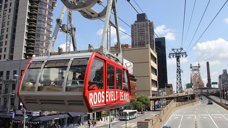 A red cable car that says "Roosevelt Island" on a line above a street