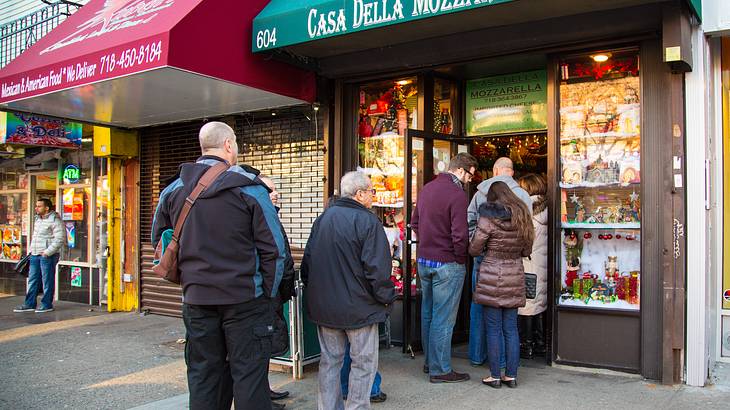 People queuing up at a small food storefront with a green awning and displays