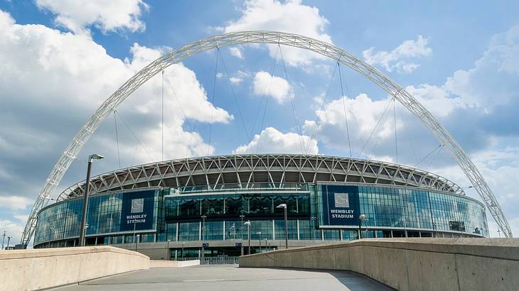 A modern sports arena with an arch structure and a sign that says "Wembley Stadium"