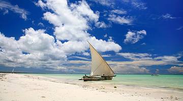 A sailboat moored in the ocean next to sand under a blue sky with white clouds