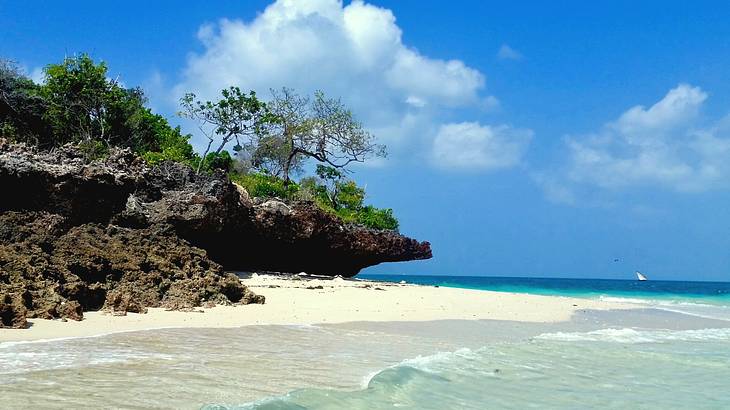 A white sand beach next to the ocean and rocks with green trees on them