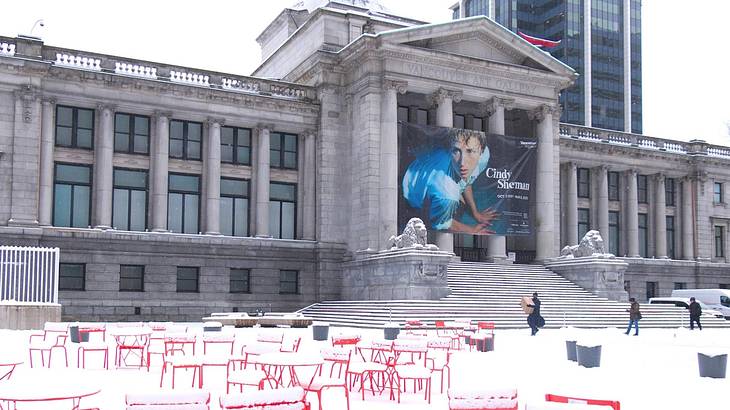 A Greek-style museum building with a banner on it and snow and chairs in front of it A Greek-style museum building with a banner on it and snow and chairs in front of it