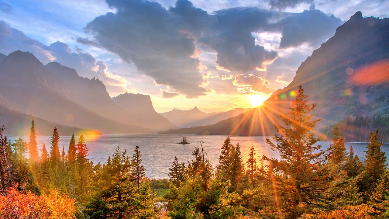 A body of water with colorful trees and mountains around it while the sun sets
