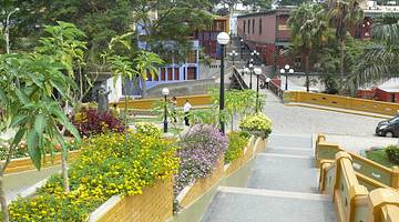 A walkway going towards a short bridge lined with streetlights, plants, and trees