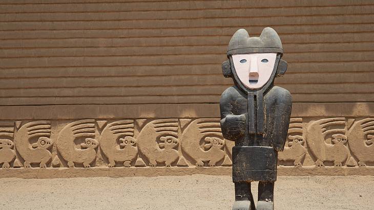 A statue of a person in front of wall carvings A statue of a person in front of wall carvings