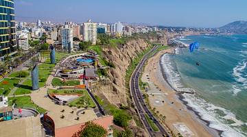 Aerial view of a beach with a cliff parallel to it with a park and buildings on top