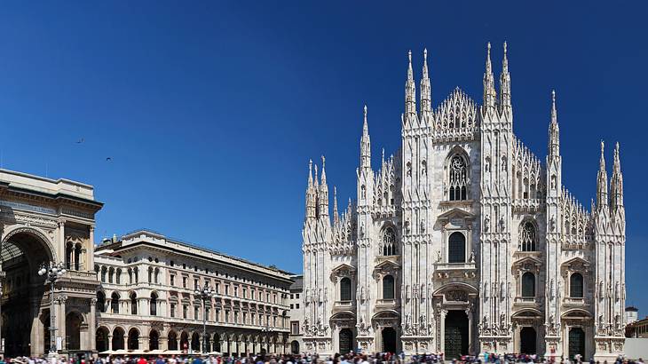 Gothic-style façade of the Milan Cathedral next to buildings on a bright sunny day