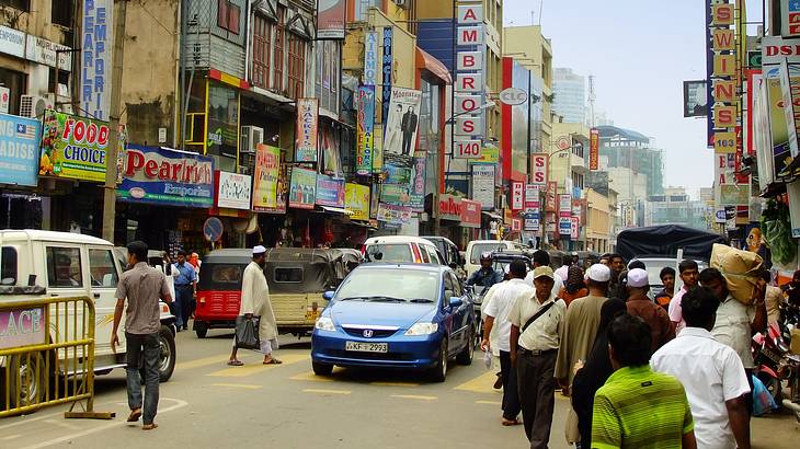 People and vehicles on a street lined with stores at Pettah Street Market