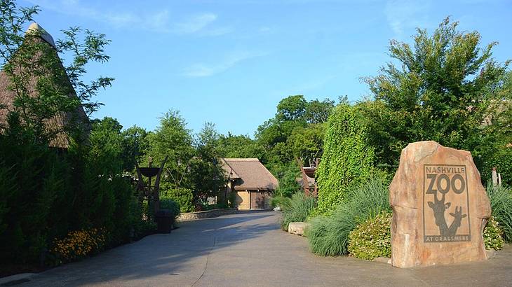 A tree-lined path with a stone sign that says "Nashville Zoo at Grassmere on it"