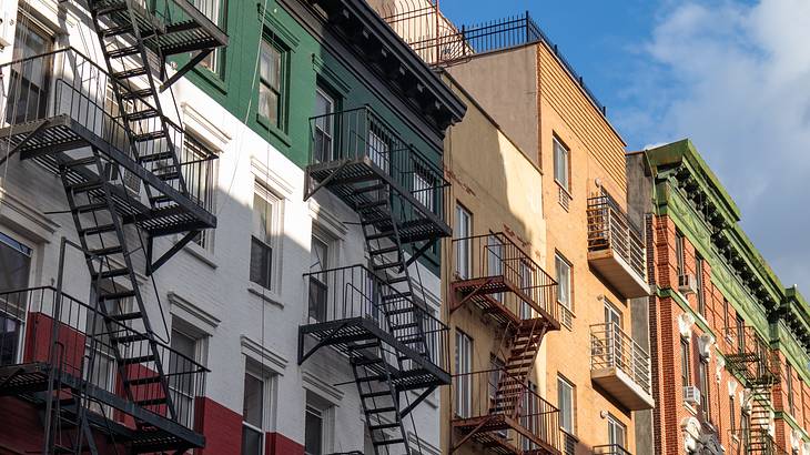 A row of apartment buildings painted green, white, and red with fire escapes