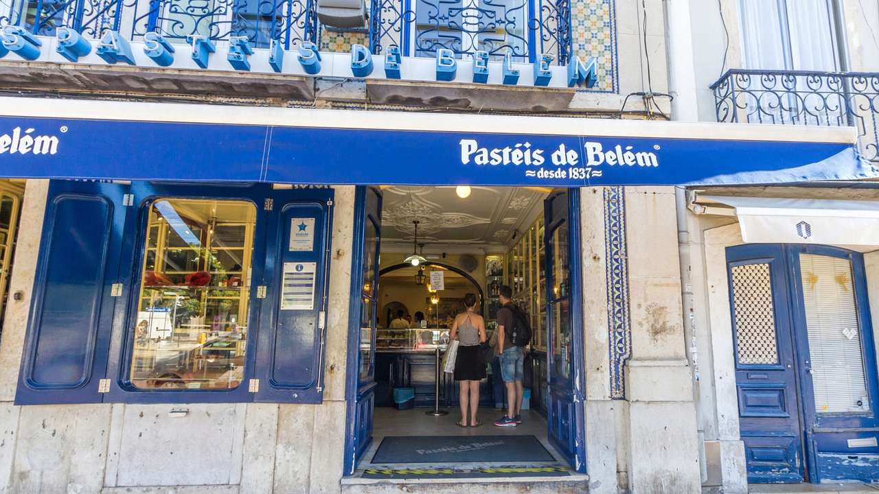 The exterior of a bakery with a blue design and a "Pastéis de Belém" sign