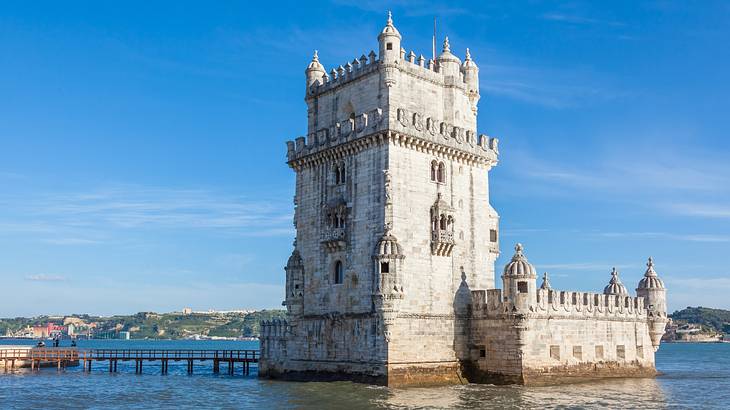 A castle-style structure within a body of water next to small hills and a blue sky