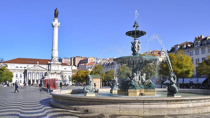 A fountain in a square with a black and white floor next to buildings and a column