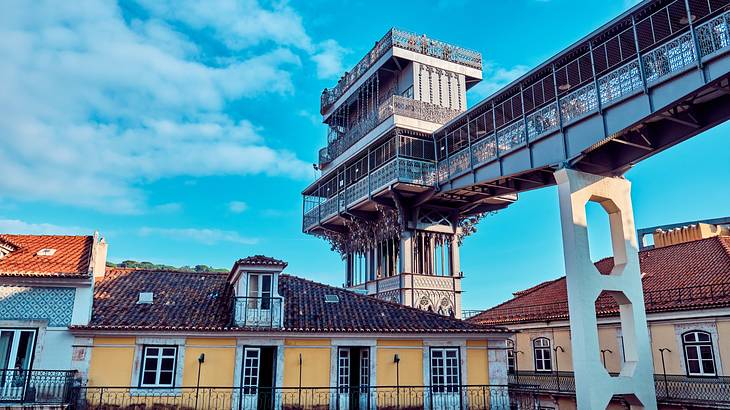 A yellow house next to a unique tower structure with a walkway under a blue sky