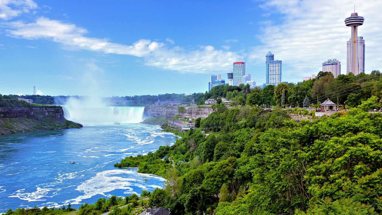 A city with buildings in the background and a waterfall with trees in front