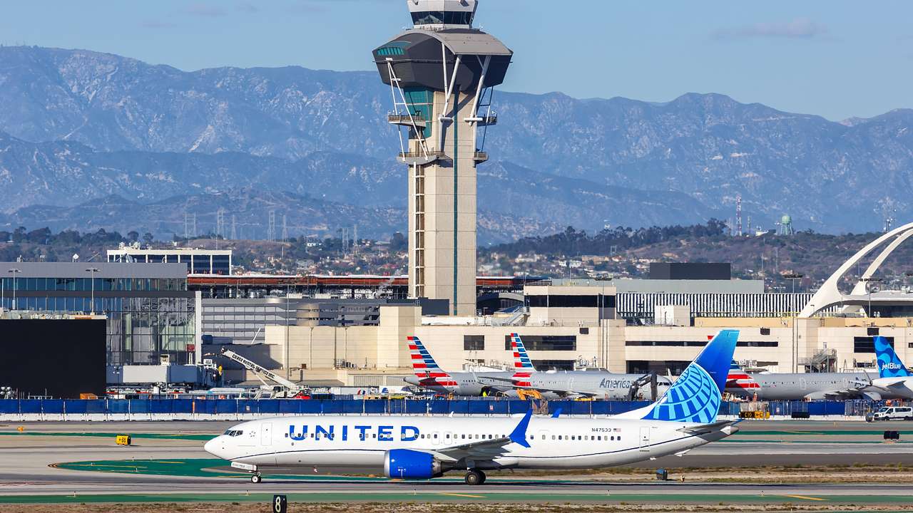 A large airplane on the runway with a tower and mountains in the background