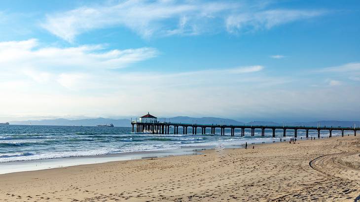 A pier and beach sand with a body of water in the distance and a clear blue sky