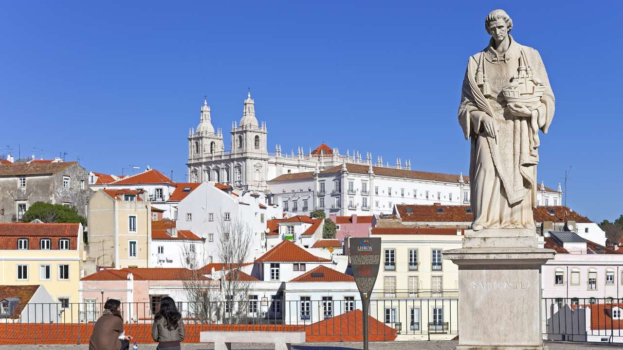 A statue of a man on a patio next to buildings with orange roofs on a clear day