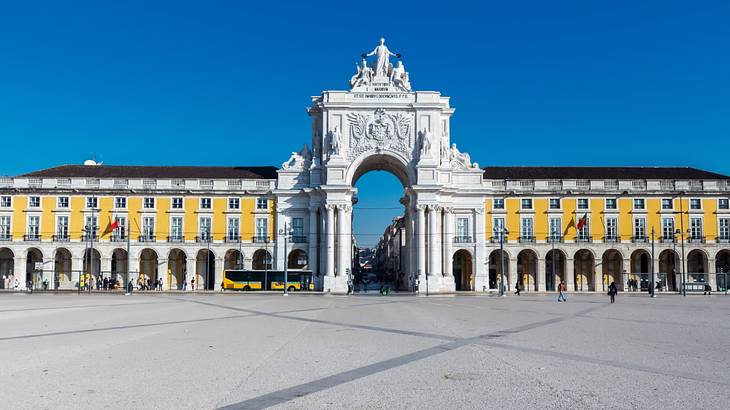 A large white arch with statues on in next to a yellow building in a square