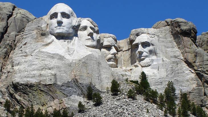 A grey rocky mountain with four large faces of men carved into it