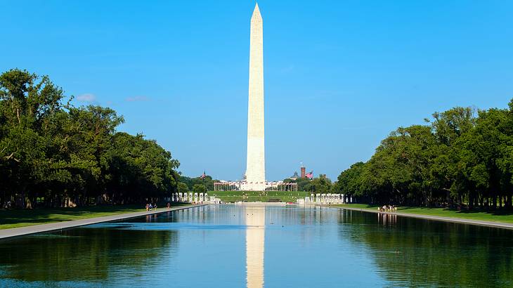 A tall white monument with a pointy top reflected in a pond