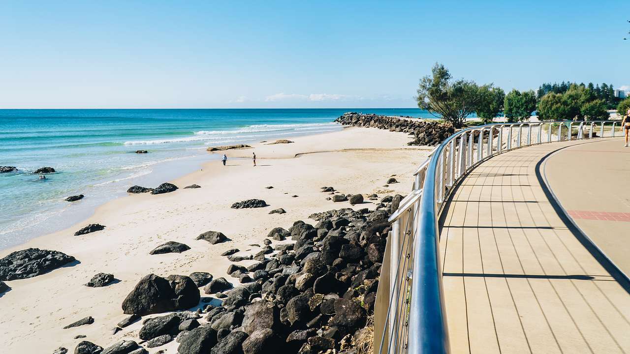 A beach with rocks and a walkway on a sunny day under clear blue skies