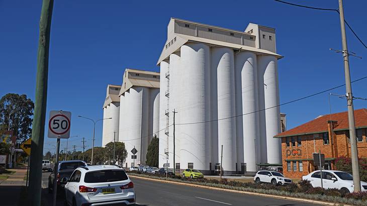 Large tall white, cylinder tower peanut silos beside a road with cars parked