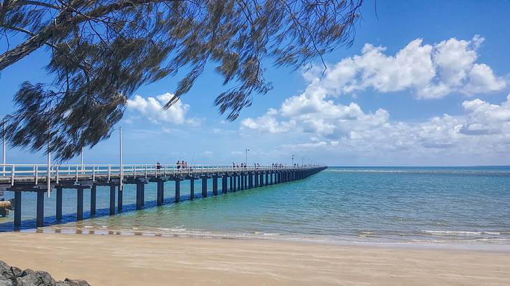 A jetty stretching into the sea from the beach under partially cloudy blue skies