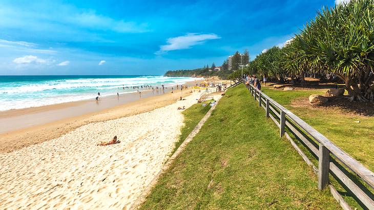 A stunning beach with blue water, white sand, and a grassy area with a fence