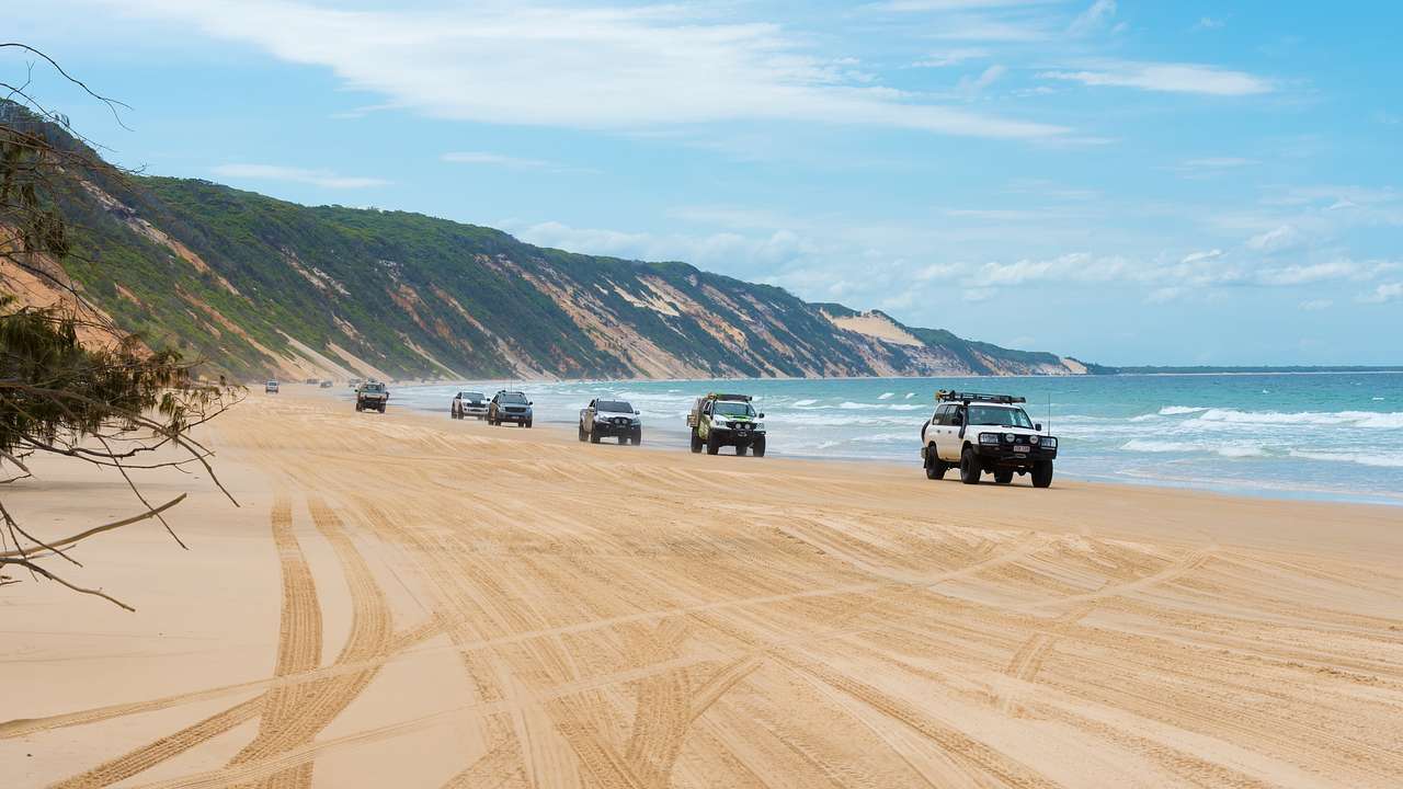 Jeeps cruising along a sandy beach with hills in back