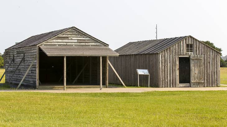 Two wooden barn-like buildings along pavement and grass
