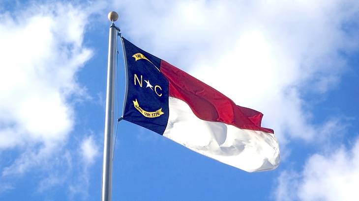 A red, white and blue flag with an emblem flying in the wind against blue sky