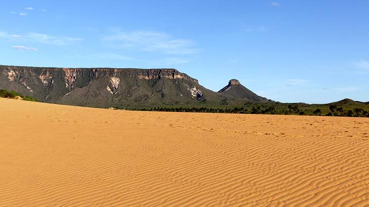 Orange-colored sand dunes with mountains at the back under a partly cloudy sky