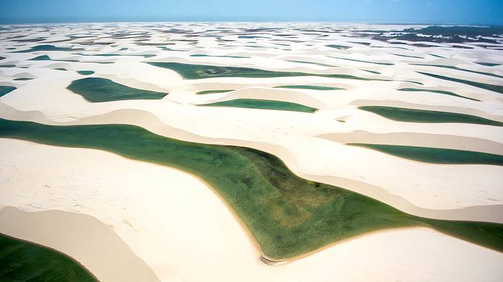 Rippling white sand dunes with greenish water in between dune peaks under a blue sky