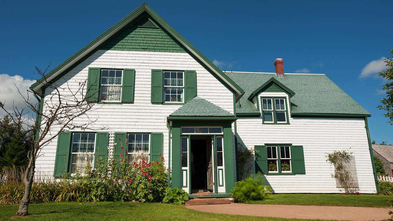 A green and white wooden house facing a green lawn on a sunny day