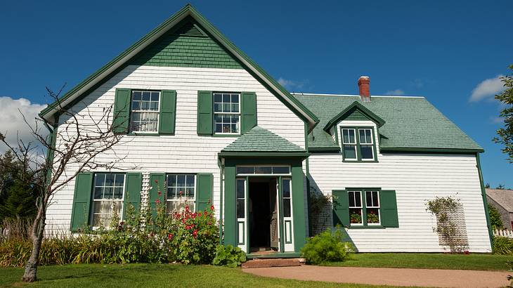 A green and white wooden house facing a green lawn on a sunny day