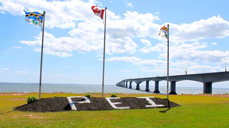 Three flags fluttering with a long bridge against a blue sky in the background