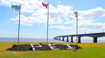 Three flags fluttering with a long bridge against a blue sky in the background