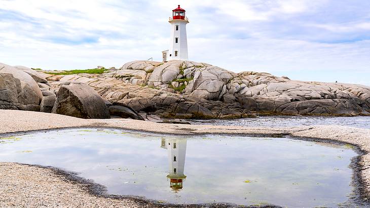 A stunning white lighthouse behind a rocky coast reflected in water below