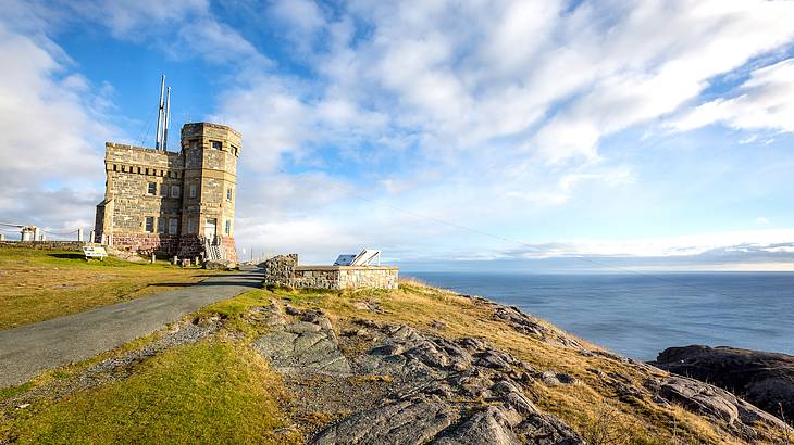 A tower on a grassy hill by the water under partially cloudy skies