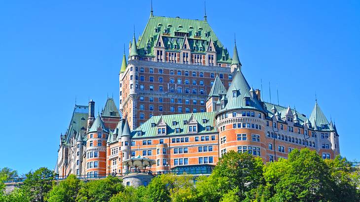 A stunning gothic castle-style building on a hill surrounded by greenery below