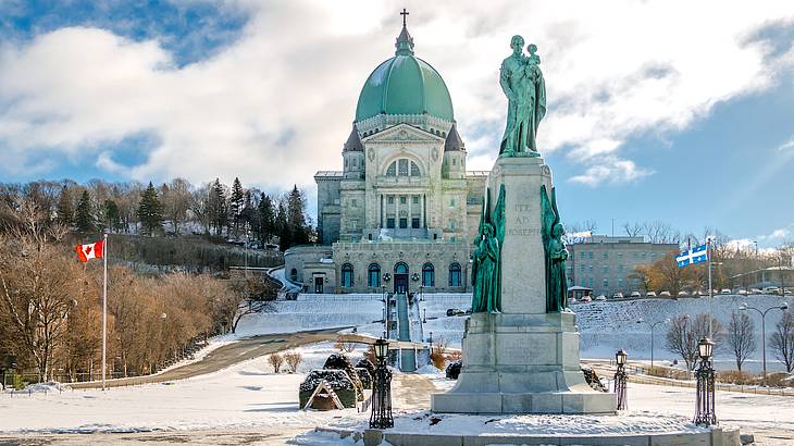 A Roman Catholic basilica with trees and a sculpture and a snow-covered lawn in front