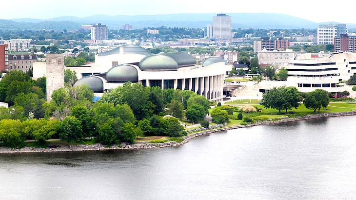 A large museum building at a waterfront with city buildings and hills behind it