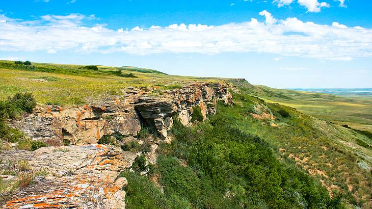 A rocky cliff surrounded by stunning green meadow and blue sky