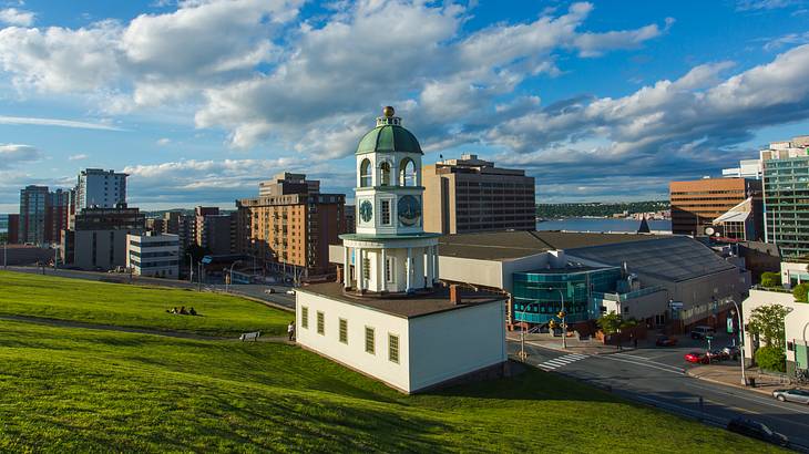 A clock tower atop a green hill with buildings in the background