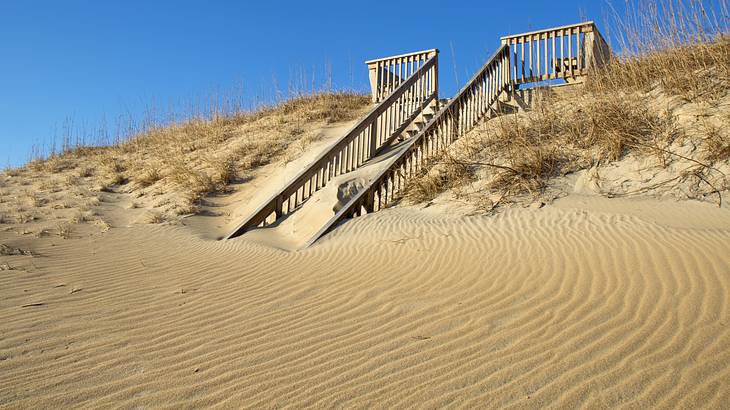 A wooden bridge over sand under a clear blue sky