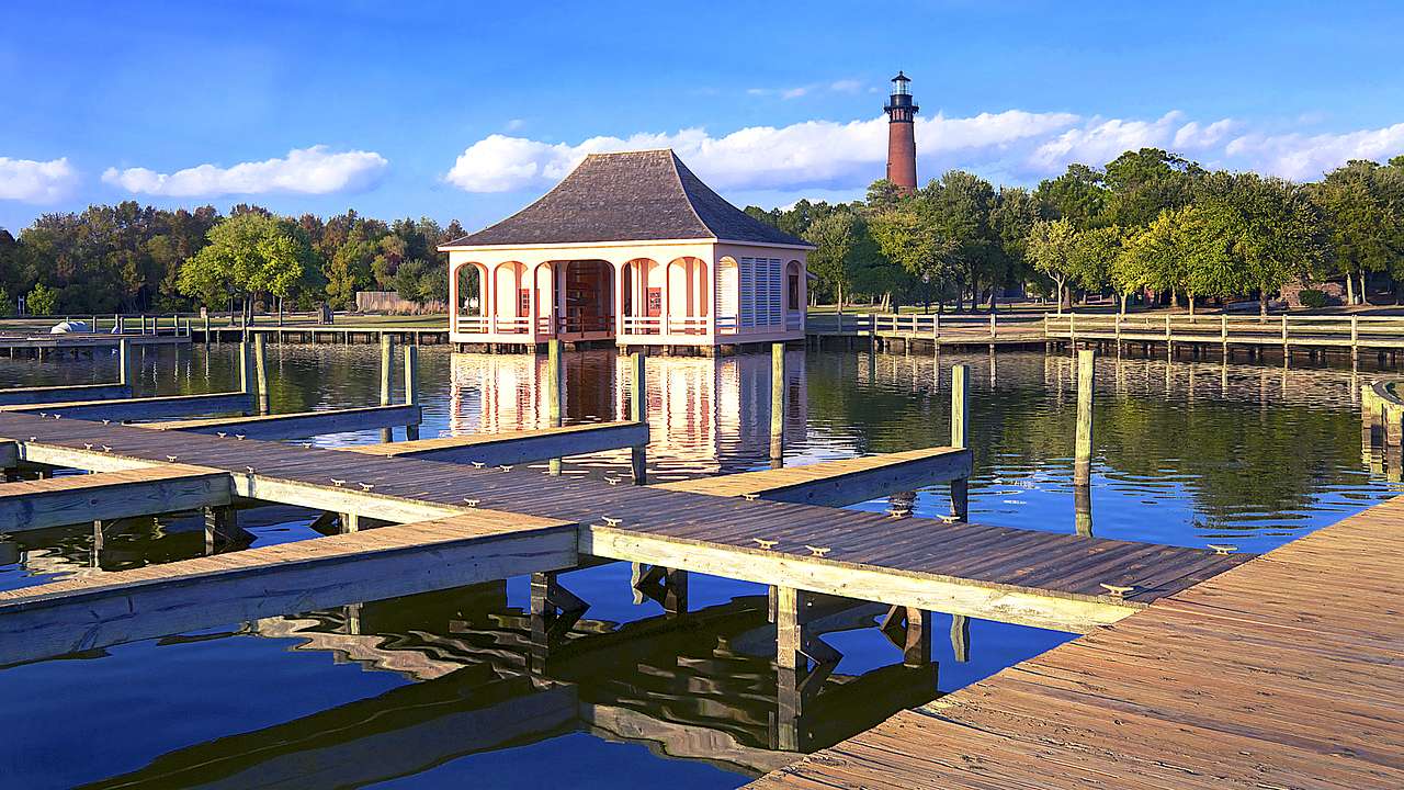 A low building surrounded by water with elevated planks and a lighthouse at the back